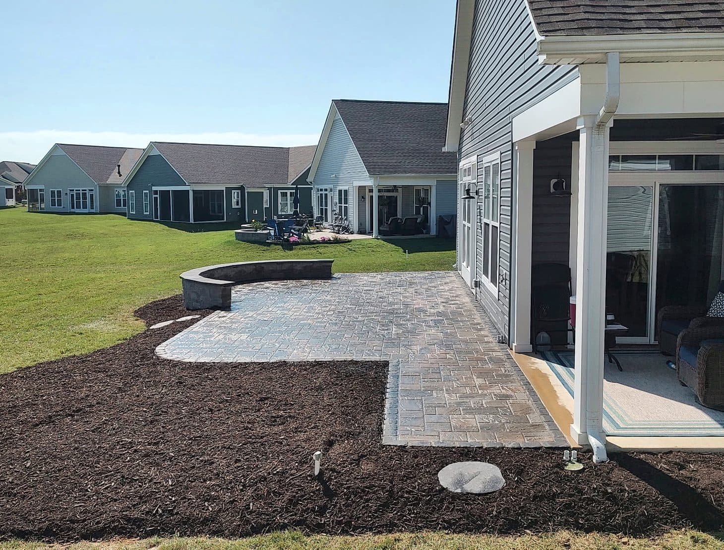 Paver patio with a curved seat wall and freshly mulched beds off a covered porch.