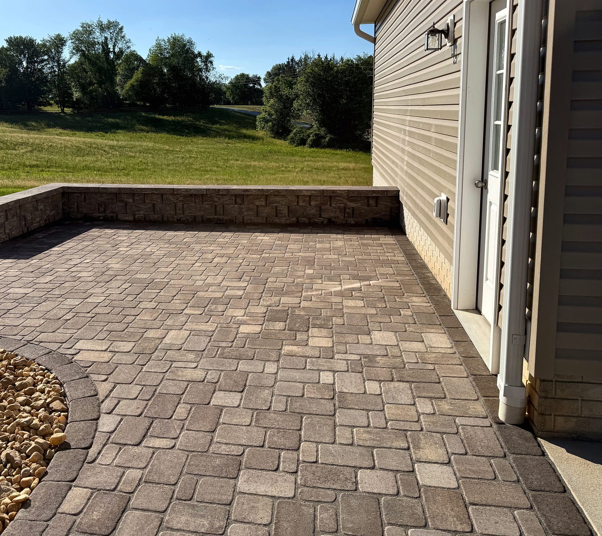 Tumbled paver patio with a low segmental seat wall overlooking an open pasture.