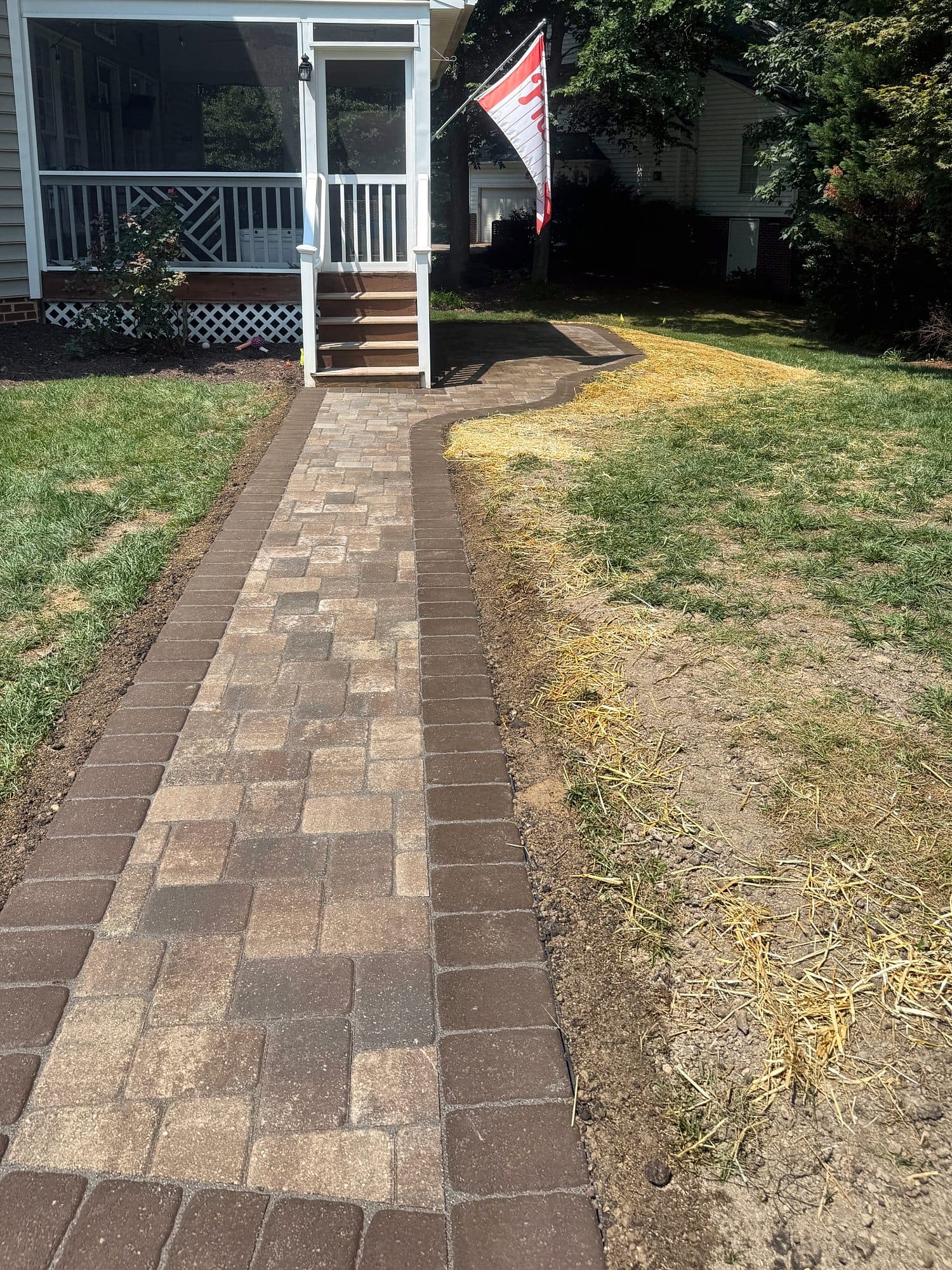 Paver walkway with a darker border leading to the steps of a screened porch.