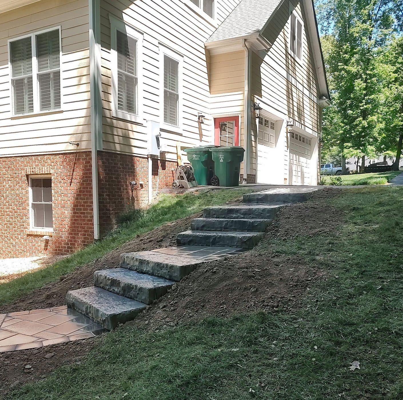 Stone slab steps and paver landings climbing a grassy slope beside a home.