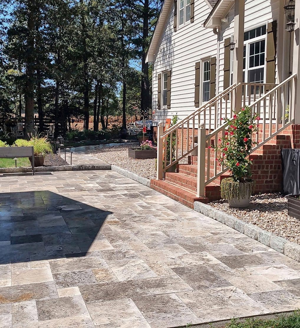 Travertine patio meeting brick steps at the back of a home, with river rock beds and planters.